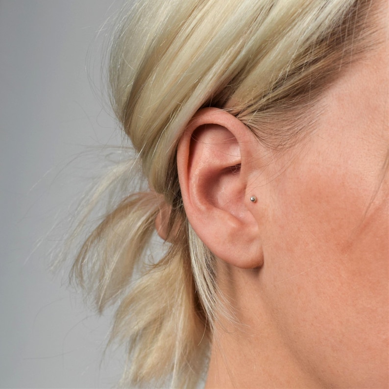 May include: A close-up of a person's ear with a small silver stud earring in the upper lobe.