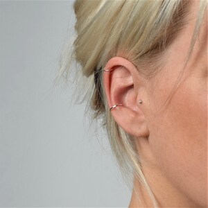 May include: A silver ear cuff and a silver stud earring in a person's ear.
