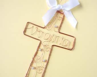 May include: A copper wire cross with the name "Virginia" spelled out in wire. The cross is decorated with white beads and a white satin bow.