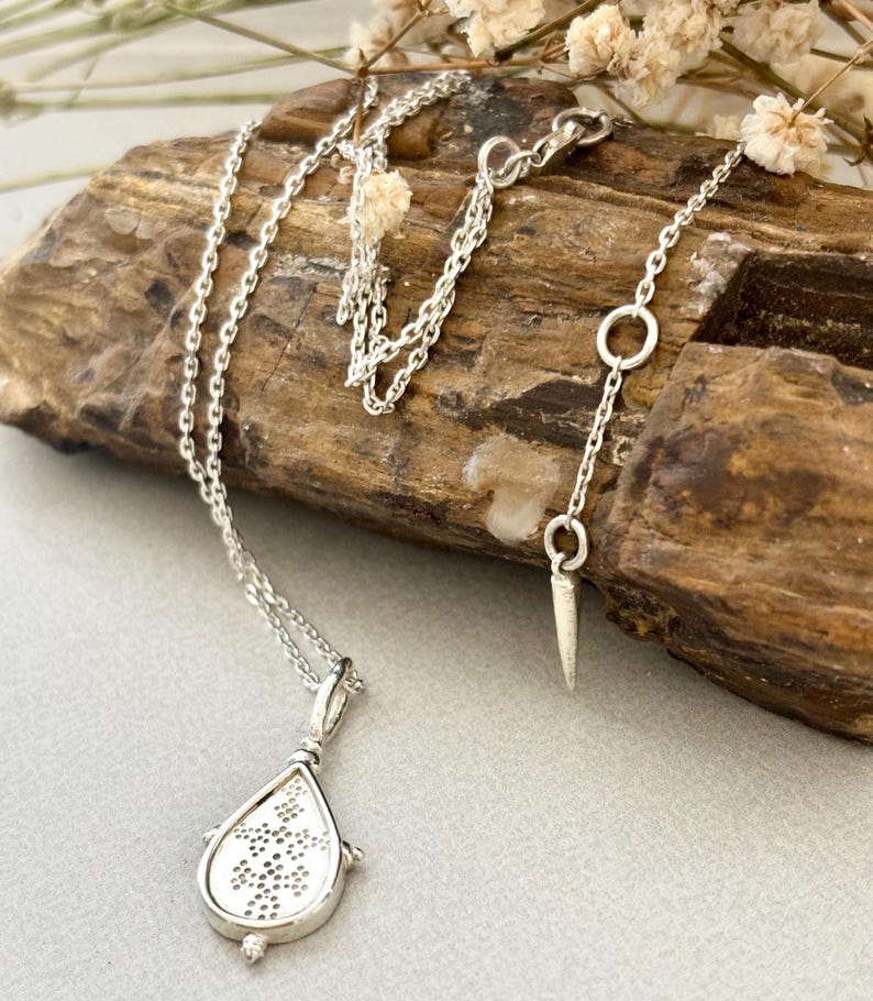 Puede incluir: Un collar de plata con un colgante en forma de l&aacute;grima que presenta un delicado y complejo patr&oacute;n. El colgante est&aacute; unido a una cadena de plata delicada.