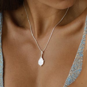 Puede incluir: Un collar de plata con un colgante en forma de l&aacute;grima. El colgante tiene un dise&ntilde;o detallado y cuelga de una cadena delicada.