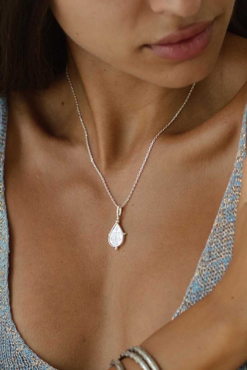 Puede incluir: Un collar de plata con un colgante en forma de l&aacute;grima. El colgante tiene un dise&ntilde;o detallado y cuelga de una cadena delicada.