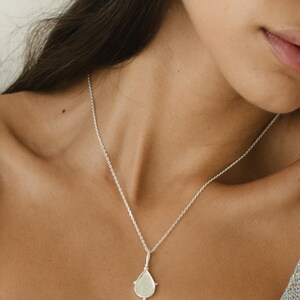 Puede incluir: Un collar de plata con un colgante en forma de l&aacute;grima y una cadena delicada. El colgante tiene una superficie texturizada y un peque&ntilde;o detalle redondo en la parte inferior.