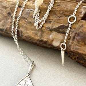 Puede incluir: Un collar de cadena de plata con un colgante en forma de l&aacute;grima. El colgante tiene un dise&ntilde;o delicado e intrincado y est&aacute; unido a una cadena de plata con un cierre de langosta.