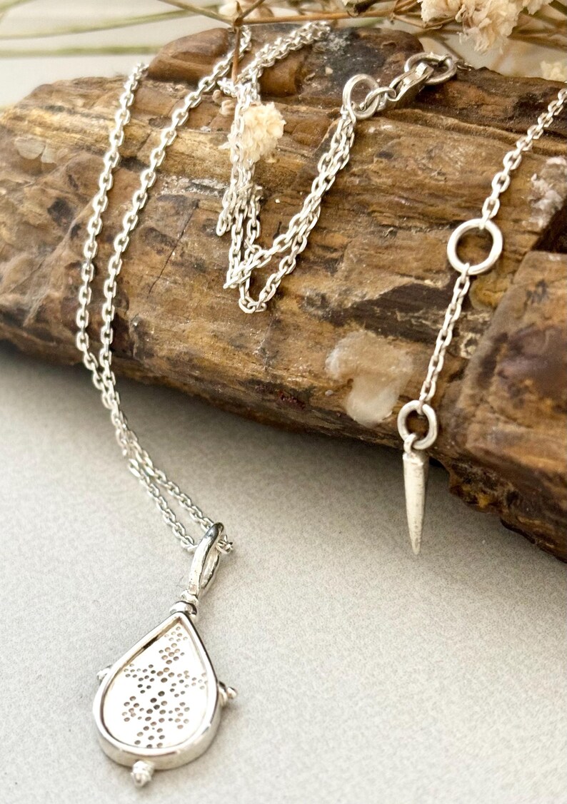 Puede incluir: Un collar de cadena de plata con un colgante en forma de l&aacute;grima. El colgante tiene un dise&ntilde;o delicado e intrincado y est&aacute; unido a una cadena de plata con un cierre de langosta.