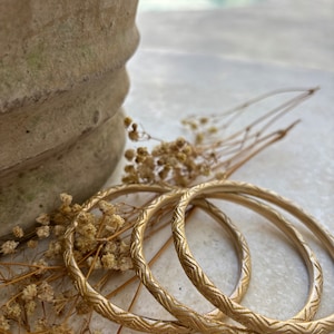May include: Three gold-colored bangles with a textured design. The bangles are stacked on top of each other.