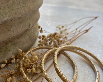 May include: Three gold-colored bangles with a textured design. The bangles are stacked on top of each other.