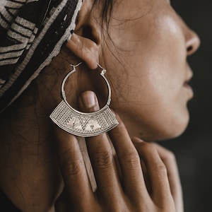 Puede incluir: Una mujer con un pañuelo estampado en la cabeza y un gran aro de plata con diseños intrincados. El arete es una pieza llamativa y agrega un toque de estilo bohemio al look.