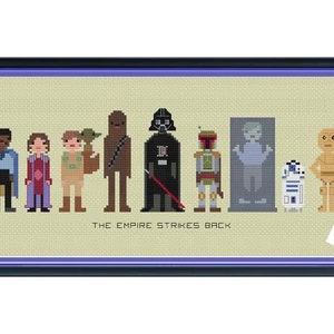 Pode incluir: Arte em ponto cruz emoldurada com personagens de "O Império Contra-Ataca". A obra apresenta figuras pixeladas de personagens icônicos como Darth Vader, Boba Fett e C-3PO. A peça é emoldurada em uma moldura preta com uma borda roxa, e o texto "THE EMPIRE STRIKES BACK" é visível.