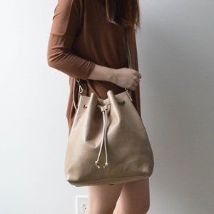 Crossbody side view of convertible leather bucket bag in sand/tan color.