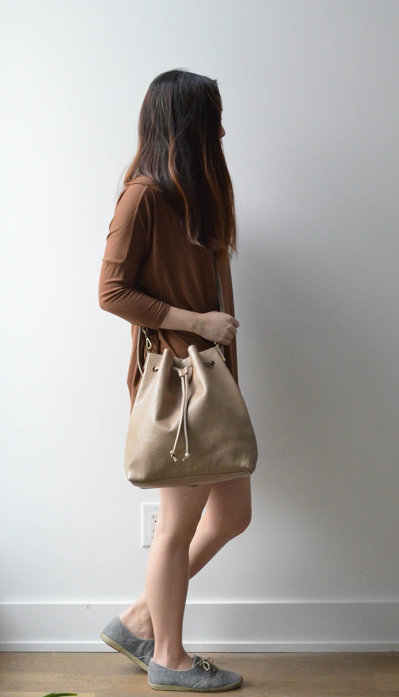 Crossbody side view of convertible leather bucket bag in sand/tan color.