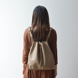 Backpack view of convertible leather bucket bag in sand/tan color.