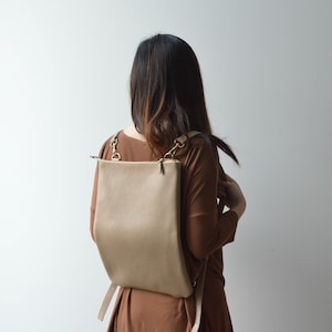 Peut inclure: Un sac à dos en cuir beige de forme rectangulaire avec une fermeture éclair. Le sac à dos est doté de bretelles réglables et d'une quincaillerie dorée. Le sac est porté sur les épaules.