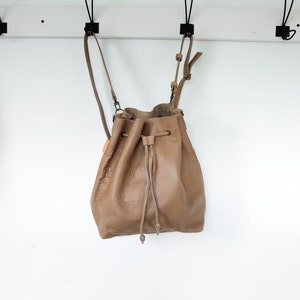 Tan colored leather backpack. Transforms from backpack to crossbody bucket bag.