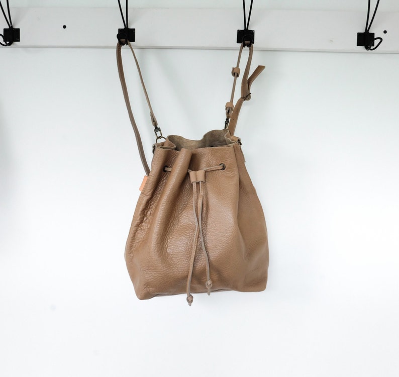 Tan colored leather backpack. Transforms from backpack to crossbody bucket bag.