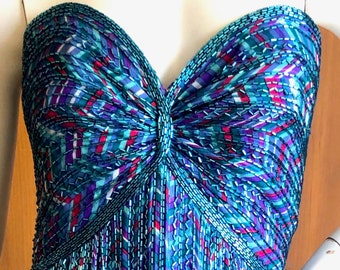 May include: A strapless, floor-length gown with a geometric pattern in shades of blue, green, purple, and pink. The gown is made of a beaded fabric and has a fitted bodice and a flowing skirt.