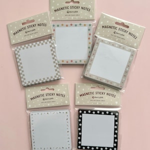 May include: Five packs of magnetic sticky notes with dry erase labels. Each pack features a different design with a white square in the center. The designs include a checkered pattern, a floral border, a border with stars and bows, a border with confetti, and a border with black and white smiley faces.