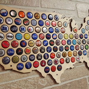 May include: A wooden map of the United States with bottle caps filling in the states. The bottle caps are various colors and brands.
