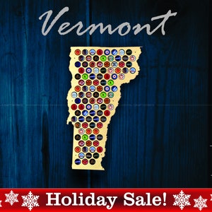 May include: A wooden cutout of the state of Vermont, painted gold, with a grid of bottle caps covering the state's shape. The bottle caps are various colors and designs. The background is a dark blue woodgrain. The text "Vermont" is written in white cursive above the state. The text "Holiday Sale!" is written in white on a red banner below the state. The text "Made in USA" is written in white on a black banner with a small American flag to the left of the text.