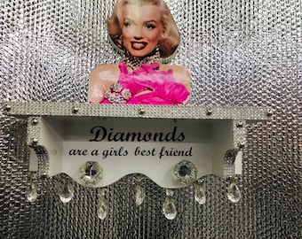 May include: A white shelf with a diamond-shaped design and the text "Diamonds are a girls best friend". The shelf has a crystal-like design and is decorated with a picture of Marilyn Monroe.