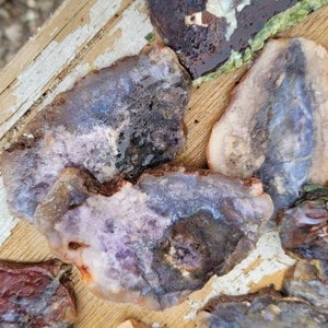 Könnte beinhalten: Eine Sammlung von Achat-Scheiben mit verschiedenen Farben und Mustern, darunter Lila, Rosa, Braun und Weiß. Die Scheiben sind auf einer Holzoberfläche angeordnet.