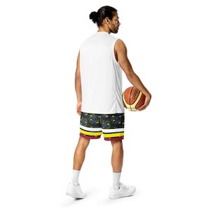 May include: A white sleeveless athletic shirt and black basketball shorts with a floral pattern of blue berries and yellow and red stripes. A basketball with brown and orange panels is held in the hand.