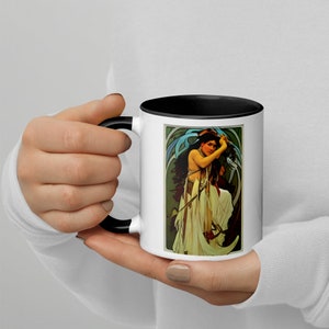 Peut inclure: Une tasse en céramique blanche avec un bord et une poignée noirs. La tasse présente une illustration colorée d'une femme en robe blanche avec un foulard bleu, tenant une épée. L'arrière-plan est un motif floral vert et bleu.