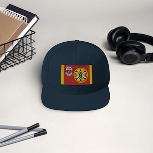 May include: A navy blue baseball cap with a red, yellow and blue flag embroidered on the front. The flag features a stylised design with a circle in the centre.