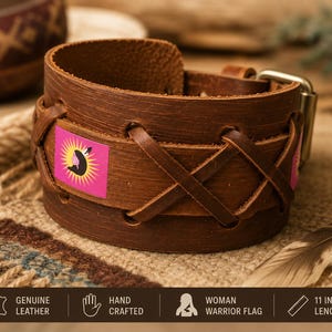 Pode incluir: Uma pulseira de punho larga de couro castanho com um design decorativo. A pulseira apresenta um patch rosa e amarelo com um gráfico preto. A pulseira tem 28 cm de comprimento e tem uma fivela de metal.