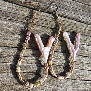 Könnte beinhalten: Ein Paar goldene Ohrringe in Tropfenform. Die Ohrringe bestehen aus einer Perlenkette und einem Anhänger aus rosa und weißem Muschelschmuck.