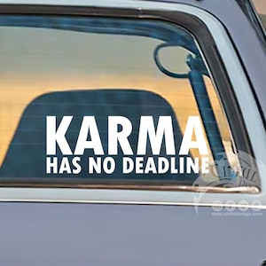 Puede incluir: Una calcomanía de vinilo blanco en la ventana de un coche con las palabras "KARMA HAS NO DEADLINE". La calcomanía está pegada en la ventana trasera de un coche gris vintage. Se ve un atardecer en el fondo.