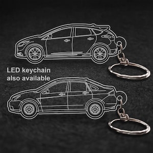 May include: Two car-shaped keyrings with silver key rings. The keyrings are white outlines of different car models. The text "LED keychain also available" is in the image. The background is black.