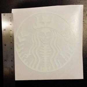 May include: White sticker with a raised design of a skeleton mermaid with long hair and a crown. The mermaid is holding a cup in each hand.