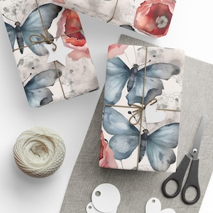 Peut inclure: Papier cadeau avec un imprimé aquarelle de papillons bleus et de fleurs de coquelicot rouges sur fond clair. Le papier est noué avec de la ficelle brune et comprend une étiquette cadeau blanche en forme d'étoile. Ficelle, ciseaux et étiquettes.