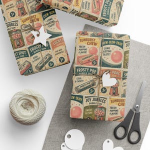 May include: Wrapping paper featuring a vintage-style graphic print of bubble gum and candy advertisements with text including Sunburst Chew, Frosty Pop, and Joy Jubbles. The paper is tied with twine and white paper tags shaped like a star and a heart.