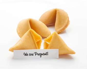 May include: Three fortune cookies, two are closed and one is open with a white paper note inside that reads "We are Pregnant!"