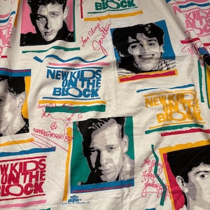 May include: A white fabric featuring a repeating pattern of New Kids on the Block band members in black and white portraits. The design includes the band name in bold green, blue, and yellow text, along with pink and red handwritten-style signatures.