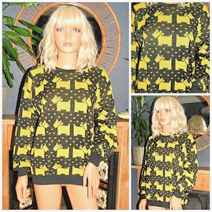 May include: A long-sleeved crew neck sweater featuring a repeating pattern of yellow Scottish terrier silhouettes against a black background, accented with small yellow heart shapes throughout the knit fabric, finished with ribbed cuffs and hem.
