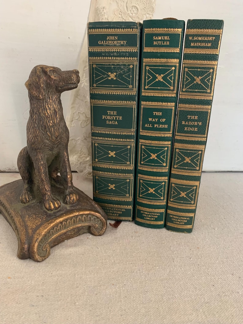 May include: A bronze dog bookend next to three vintage books with green covers and gold lettering. The books are titled "The Forsyte Saga", "The Way of All Flesh", and "The Razor's Edge". The bookend is on a decorative base.