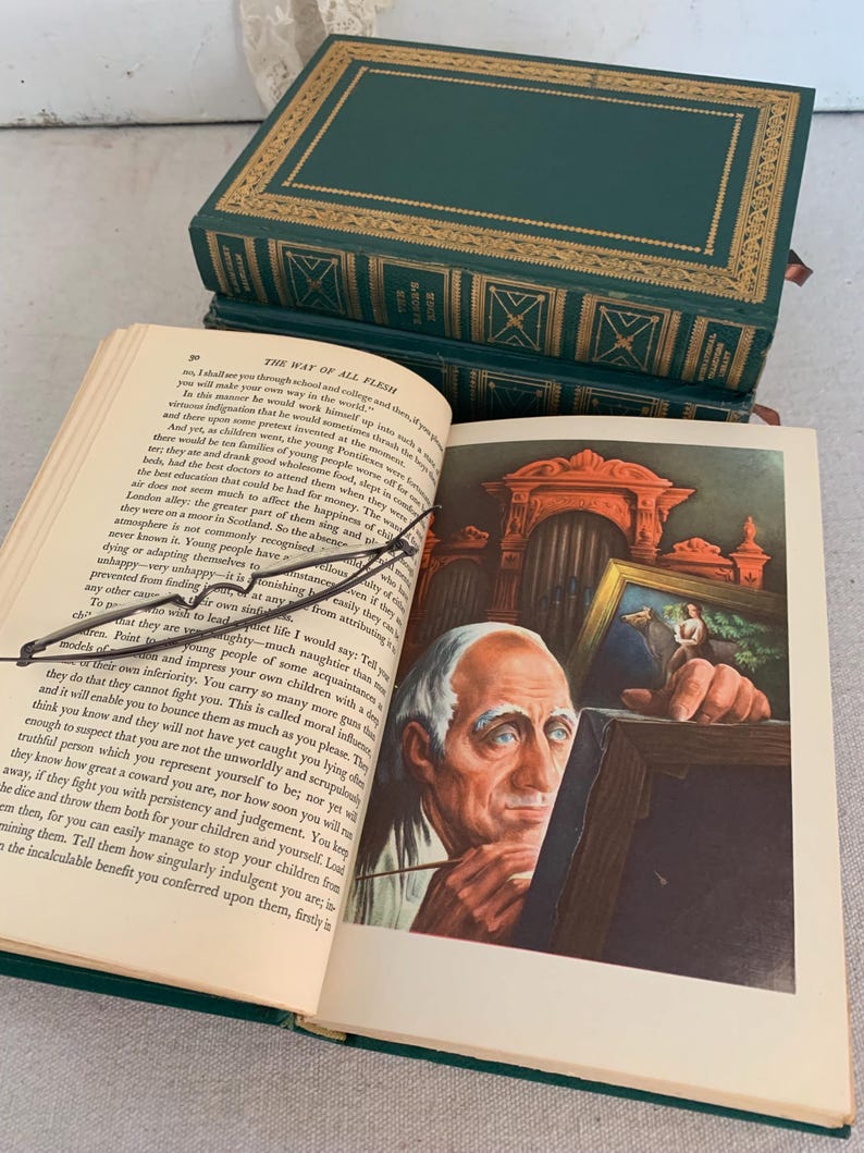 May include: An open book with an illustration of an elderly man painting. The book is titled "The Way of All Flesh" and is bound in dark green leather with gold detailing. Two more books are stacked behind it.