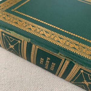 May include: Close-up of a hardcover book titled "The Razor's Edge." The book has a dark green cover with gold decorative accents and text. The edges of the book are also green with gold detailing. The book appears to be vintage.