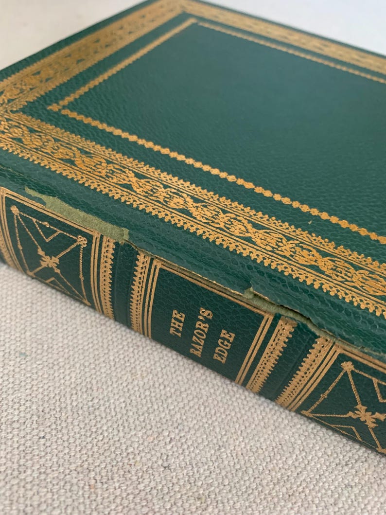 May include: Close-up of a hardcover book titled "The Razor's Edge." The book has a dark green cover with gold decorative accents and text. The edges of the book are also green with gold detailing. The book appears to be vintage.