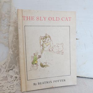 May include: Vintage children's book titled "The Sly Old Cat" by Beatrix Potter. The cover features a color illustration of a cat and mouse at a table. The book has a cream-colored cover with pink text.