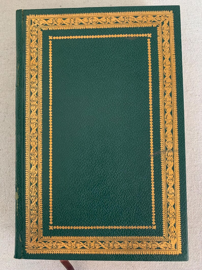 May include: A hardback book with a dark green cover and gold decorative border. The cover has a textured appearance. The gold border features an intricate design. A red ribbon bookmark is visible.