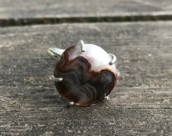May include: A silver ring with a brown and white agate stone set in a prong setting.