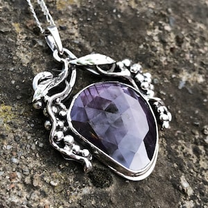May include: A silver pendant necklace featuring a large, faceted, purple gemstone set within a silver vine design.