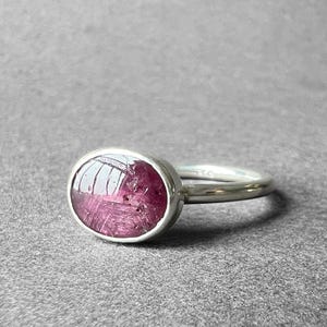 May include: A silver ring with a pink oval-shaped gemstone set in the centre.