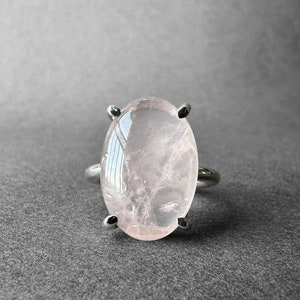 May include: A silver ring with a large oval-shaped rose quartz gemstone. The ring has a simple design with four prongs holding the stone in place.