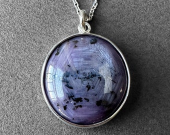 Op de afbeelding: Een zilveren ketting met een ronde hanger met een paarse en zwarte edelsteen.