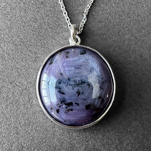 May include: A silver chain necklace with a round pendant featuring a purple and black gemstone.